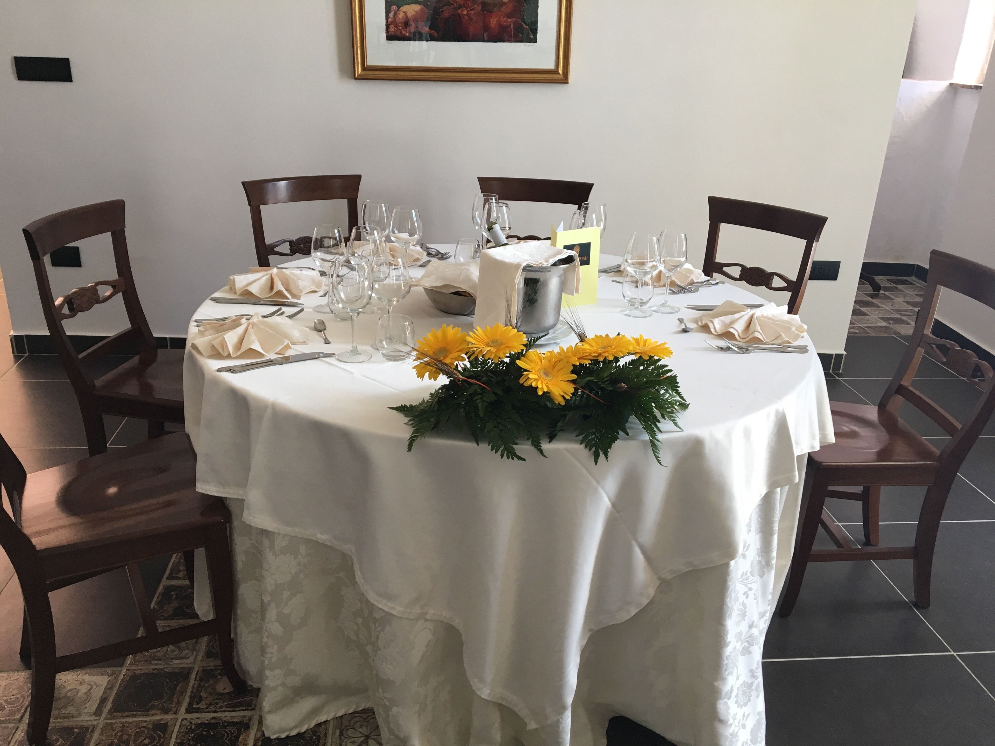 A round dining table set with white tablecloth, chairs, and a centerpiece of yellow flowers.