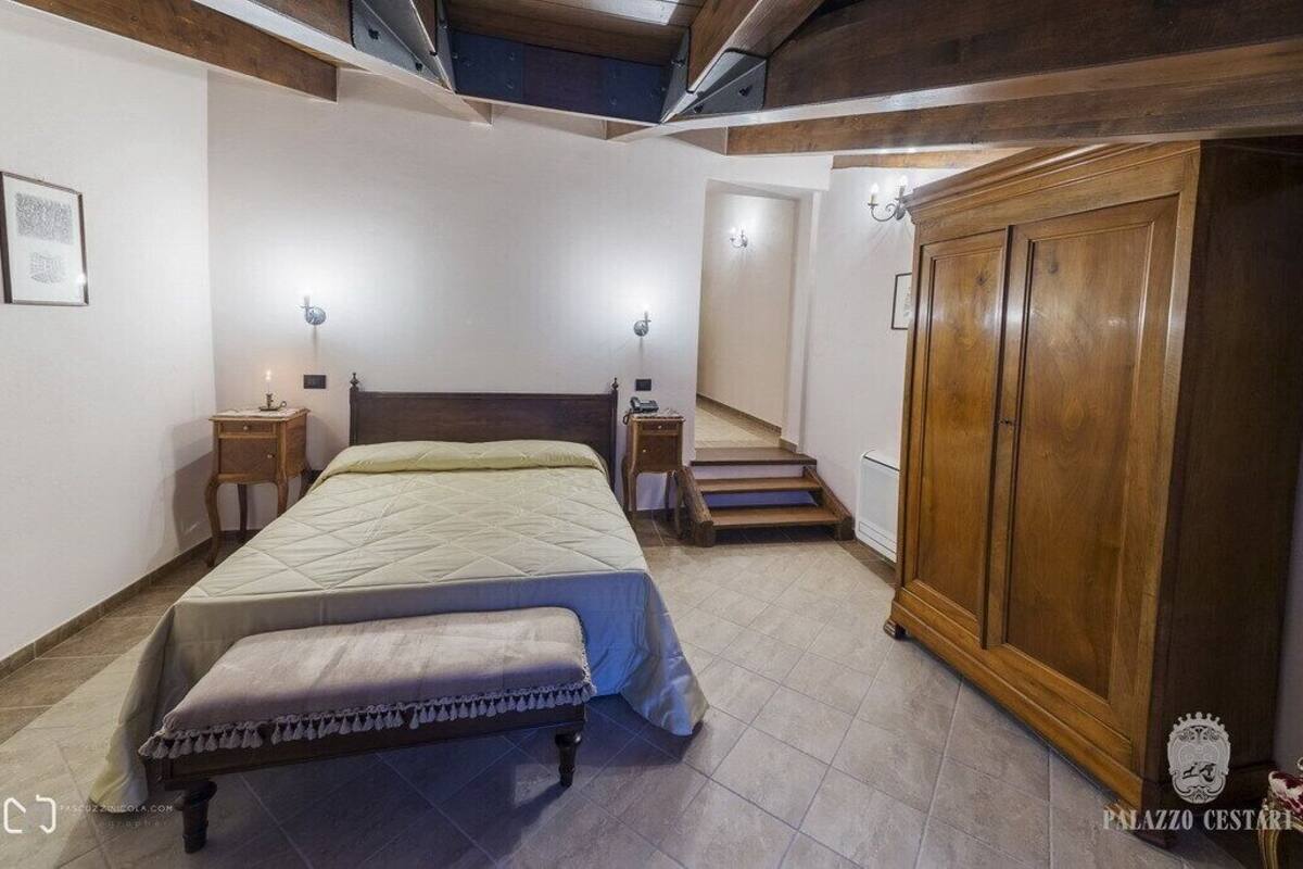 A bedroom with a bed, bedside tables, a wardrobe, and a staircase leading to another room.