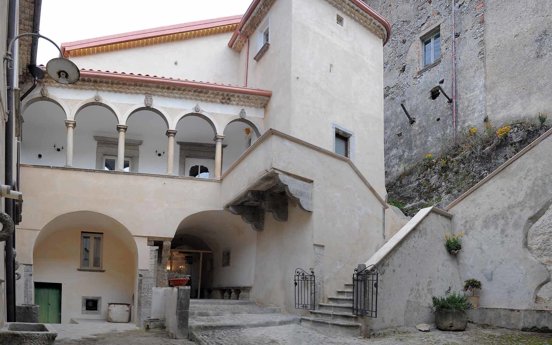 A courtyard with a building featuring arched walkways and a staircase leading to an upper level.