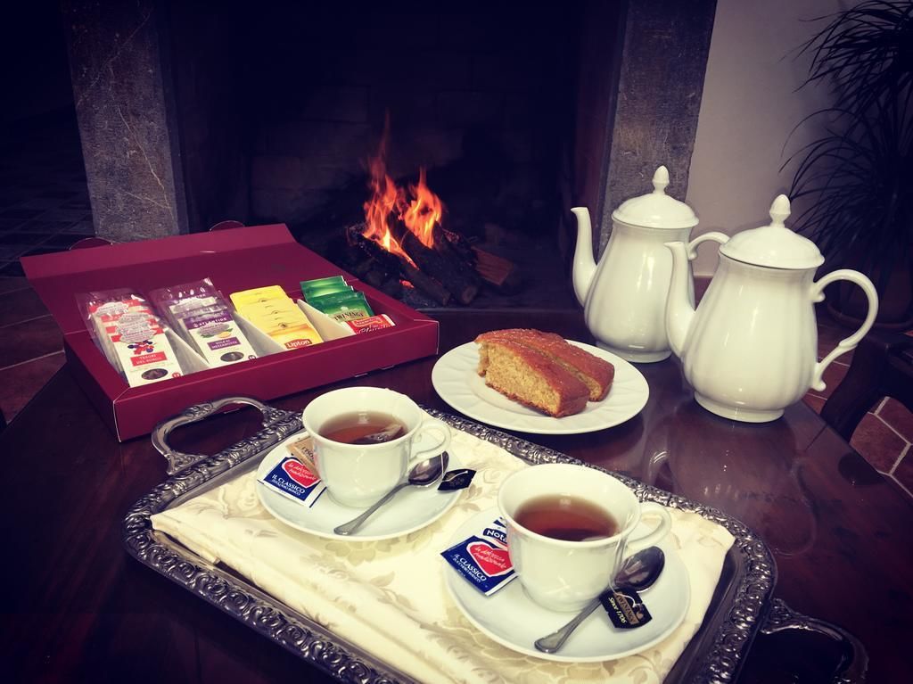 A tray with two cups of tea, a teapot, a sugar bowl, a box of tea bags, and a slice of cake on a table near a fireplace.