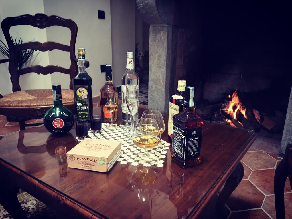 A wooden table with liquor bottles, glasses, and a box of Plantation rum. A fireplace with burning logs is in the background.