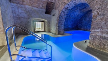Un área de spa con una piscina azul, un ventanal de cristal y un arco de piedra.