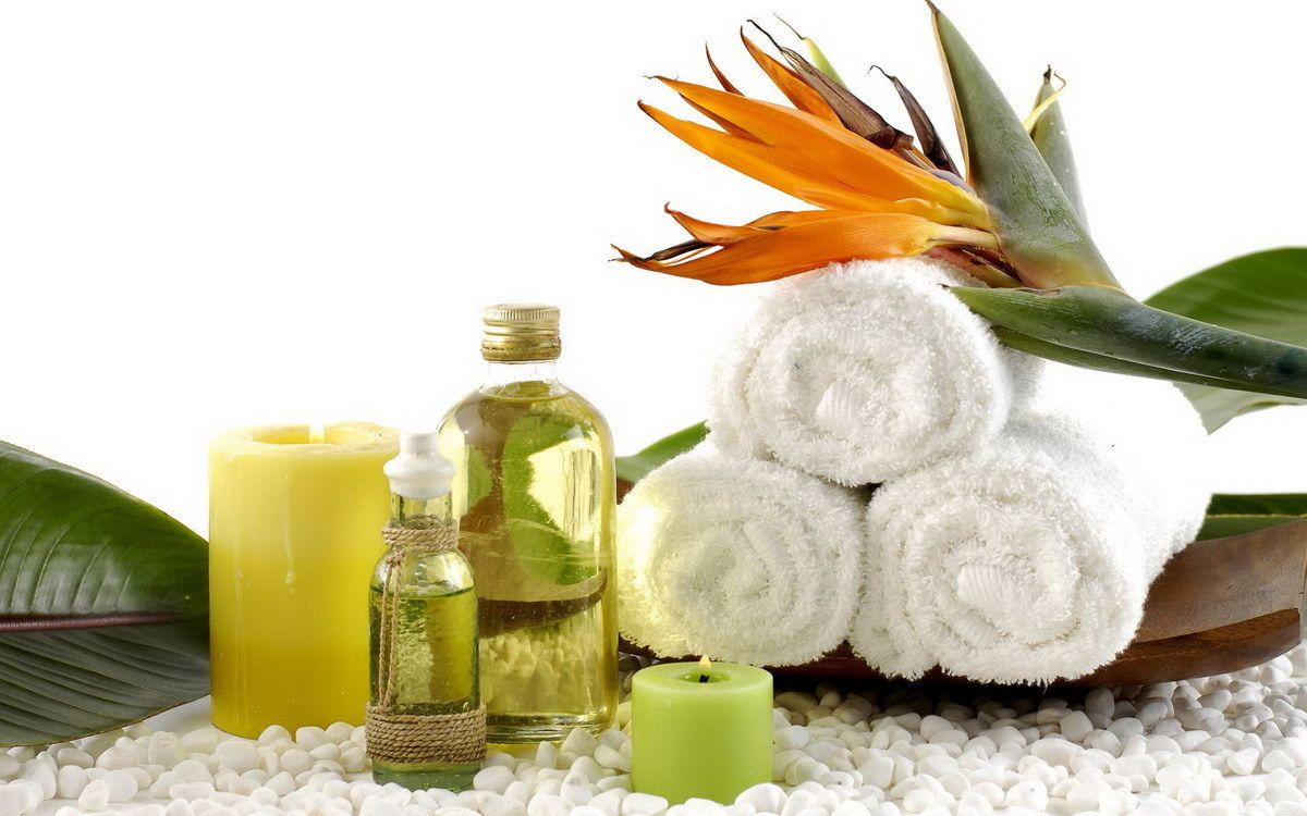 A spa setting with a flower, candles, and rolled towels on white pebbles.
