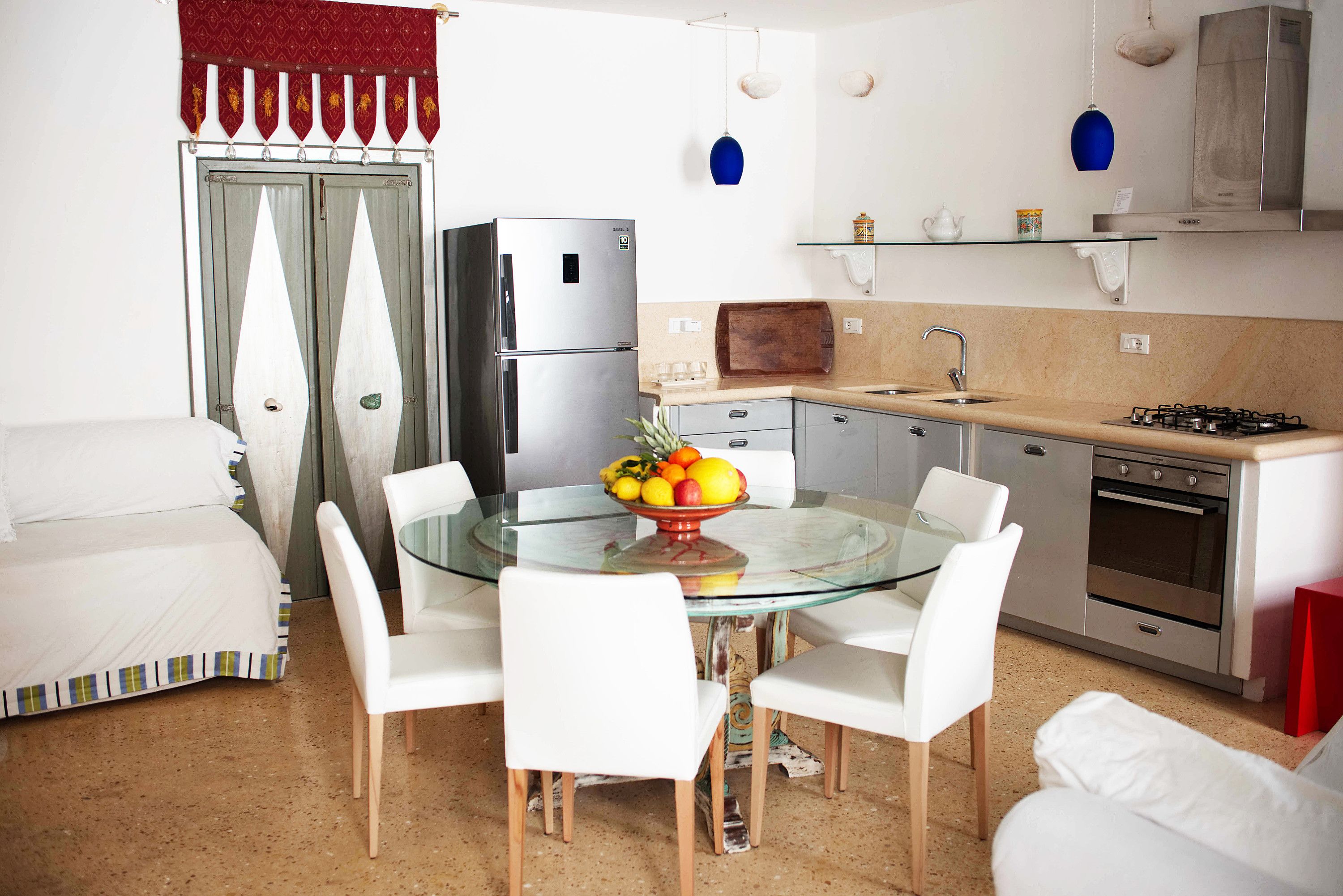 A modern kitchen with a glass dining table, white chairs, a refrigerator, a stove, and a sink.