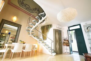A modern interior with a spiral staircase, a dining area with white chairs, and a large mirror. - Salapolis Luxury Apartments (Gallipoli)