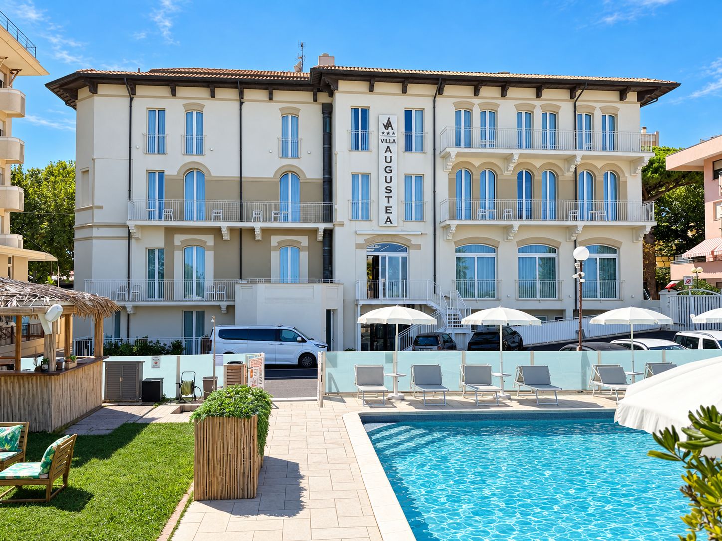 Un hotel su più piani con piscina, area salotto esterna e un cartello che indica 'VILLA AUGUSTA'.