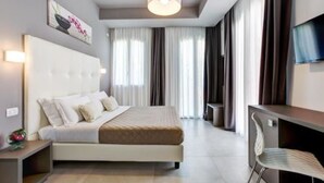 A modern hotel room with a large bed, a desk, and a chair. There is a TV on the wall and a window with curtains. - Villa Augustea (Rimini)