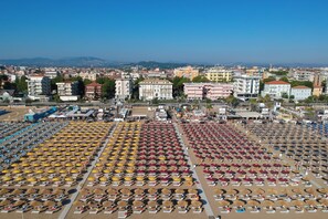 A beach with rows of umbrellas and sun loungers, a marina with boats, and buildings in the background. - Villa Augustea (Rimini)