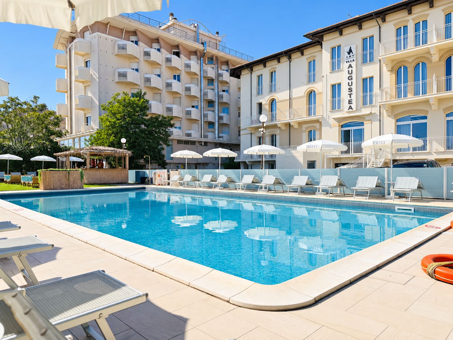 Una piscina con lettini e ombrelloni, circondata da edifici a più piani con balconi.