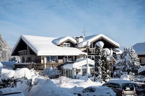 Een besneeuwde lodge met een groot dak, meerdere ramen en een zichtbare schoorsteen.