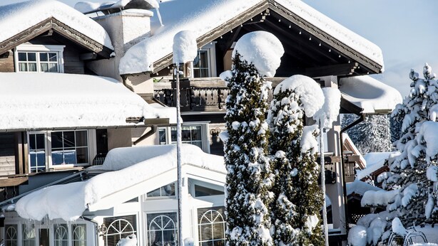 A snow-covered lodge with multiple balconies and a ski lift visible in the background.