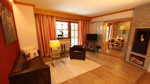 A cozy living room with a fireplace, a sofa, a television, and a dining area visible through an open door.