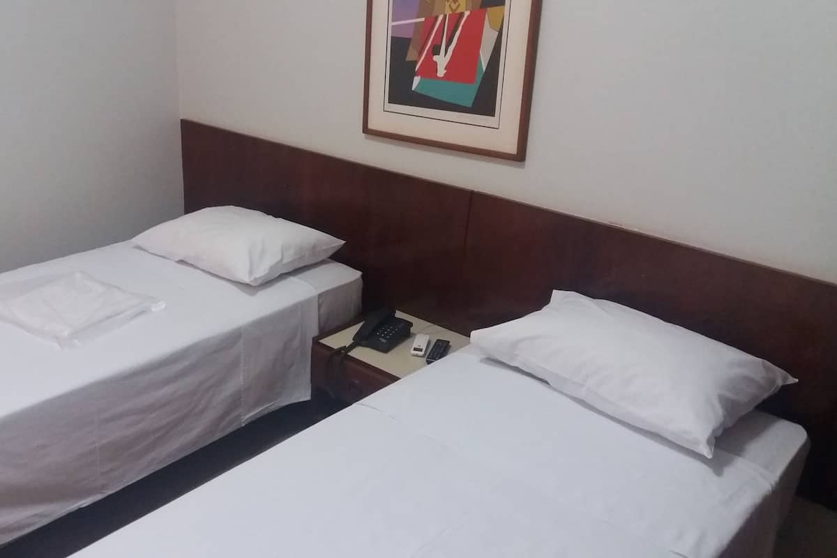 A hotel room with two single beds, each with white linens and pillows. There is a framed picture on the wall above the beds.