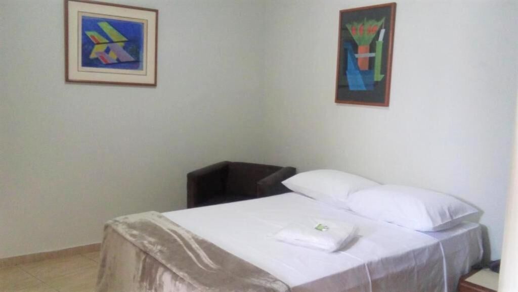 Una habitación sencilla con una cama, una silla y dos obras de arte enmarcadas en las paredes.