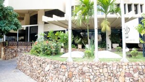 Un hotel con pared de piedra, palmeras y diversas plantas.