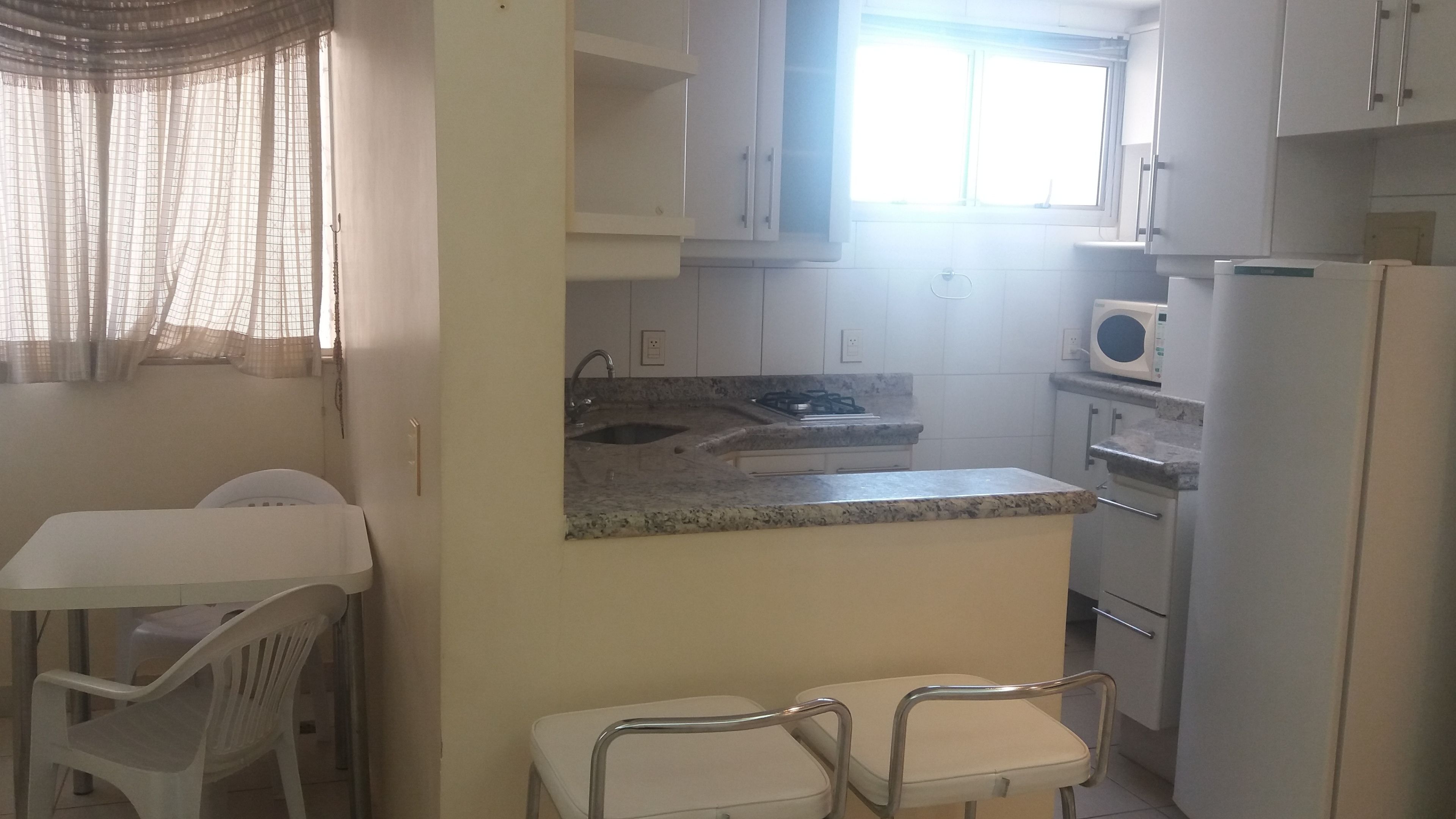 Cocina compacta con pileta, cocina y microondas. Pequeño comedor con dos sillas y una mesa.