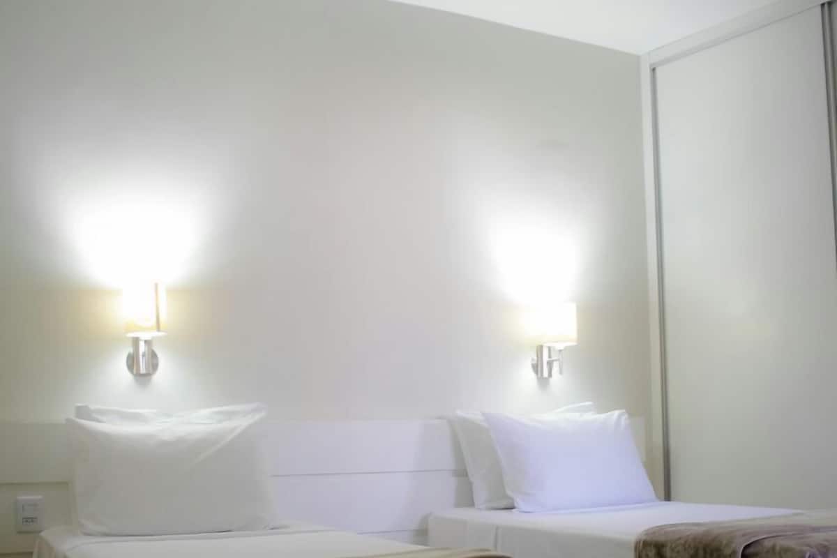 A hotel room with two beds, each with white linens and a bedside lamp.