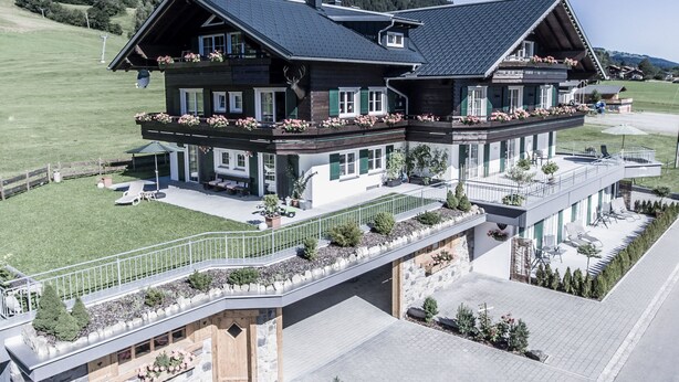 Un grand chalet à deux étages, doté d’un balcon, d’une terrasse couverte et de fondations en pierre.
