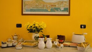 Una mesa de comedor con diversos alimentos y un jarrón de flores amarillas frente a una pared amarilla.