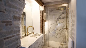 Un baño con lavamanos de mármol, ducha con cerramiento de vidrio y pared de ladrillo.