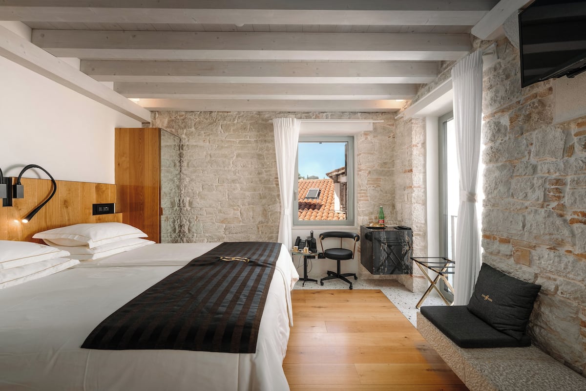 Un dormitorio con dos camas, un escritorio de madera, una silla y una pared de piedra.