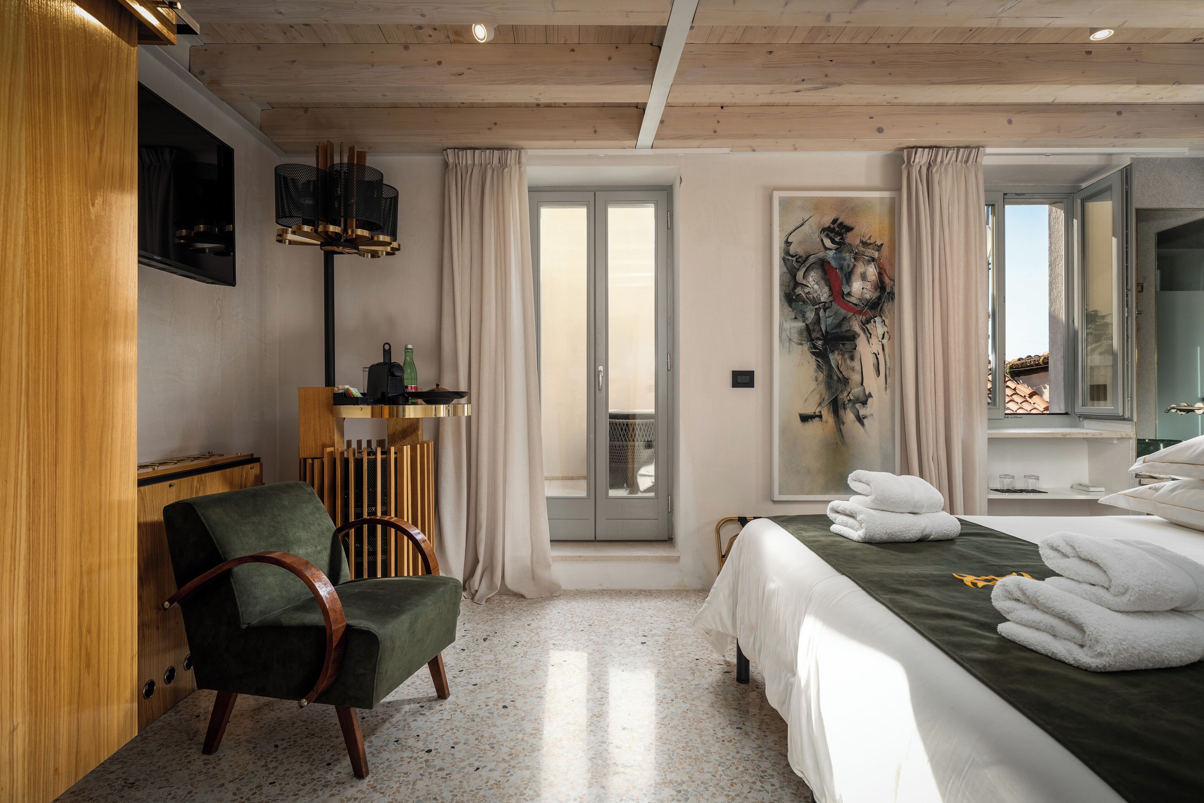 A hotel room with a bed, a chair, a desk, a TV, and a view of the outside.
