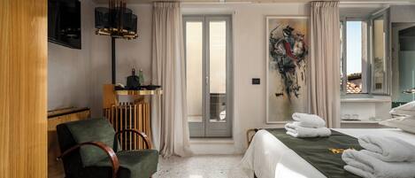 A hotel room with a bed, a chair, a desk, a TV, and a view of the outside.
