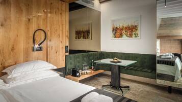 Habitación de hotel con cabecera de madera, un banco tapizado en verde, una mesita de vidrio y una cama con ropa de cama blanca.