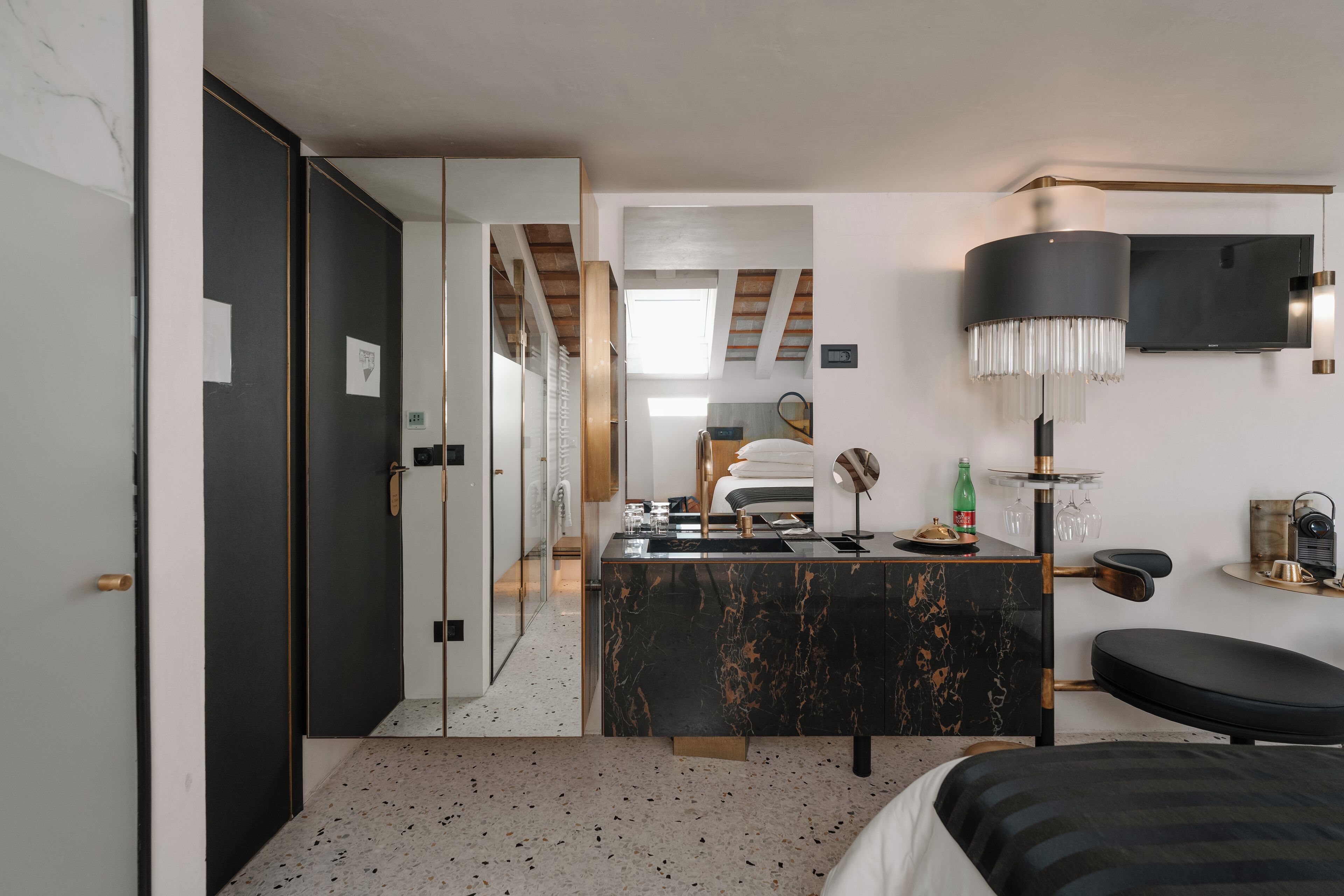 Una habitación de hotel moderna con baño de mármol, una cama grande, un área de descanso y un televisor montado en la pared.