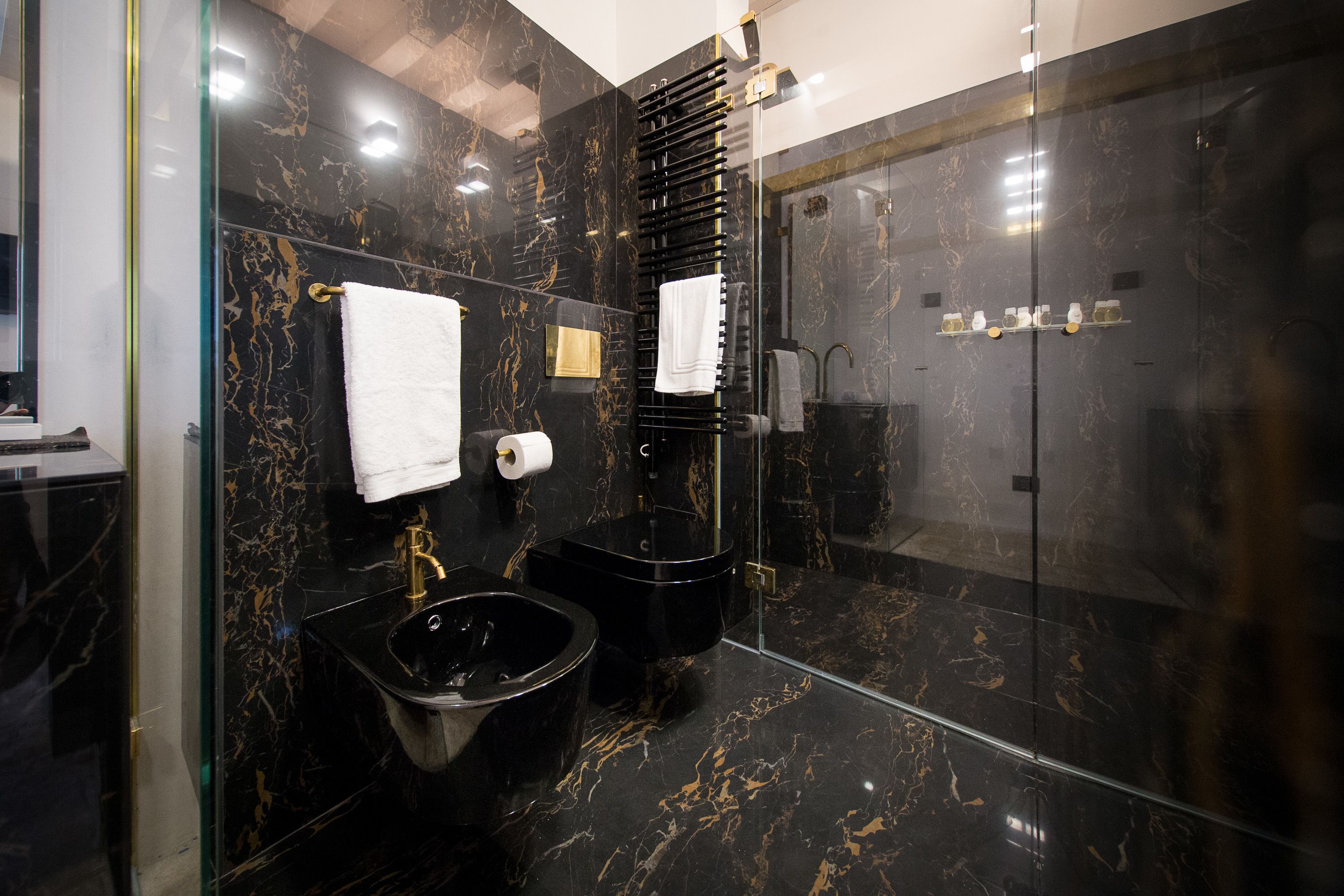 A modern bathroom with a black marble sink, a black bidet, and a glass-enclosed shower.