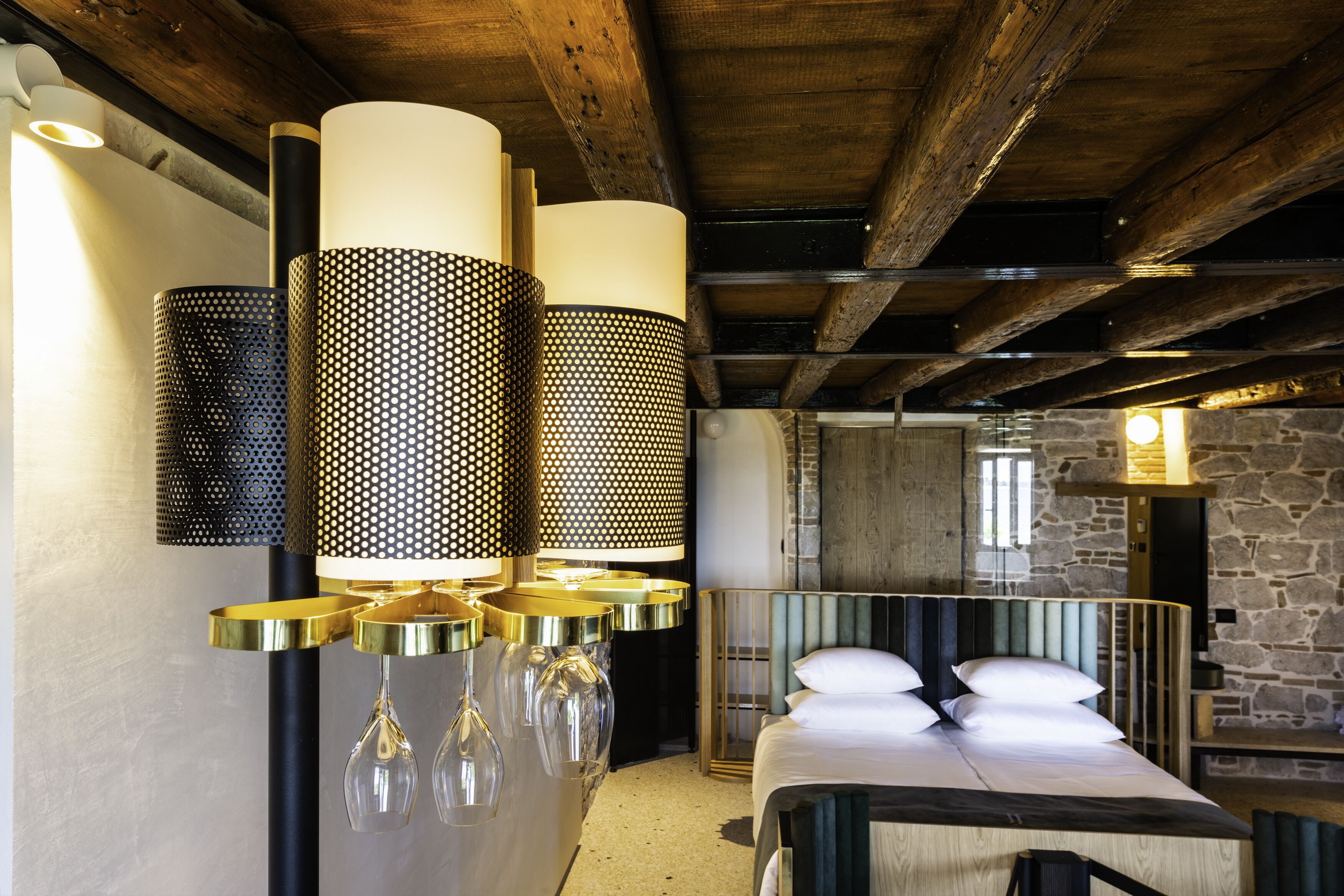 Una habitación de hotel moderna con techo de madera, cama con cabecera verde y varias lámparas de pie con diferentes pantallas.
