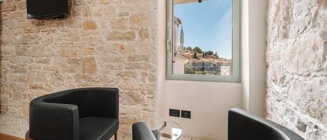 Una habitación con pared de piedra, sofá de cuero negro, mesa de centro de vidrio y ventana con vista a un paisaje urbano.