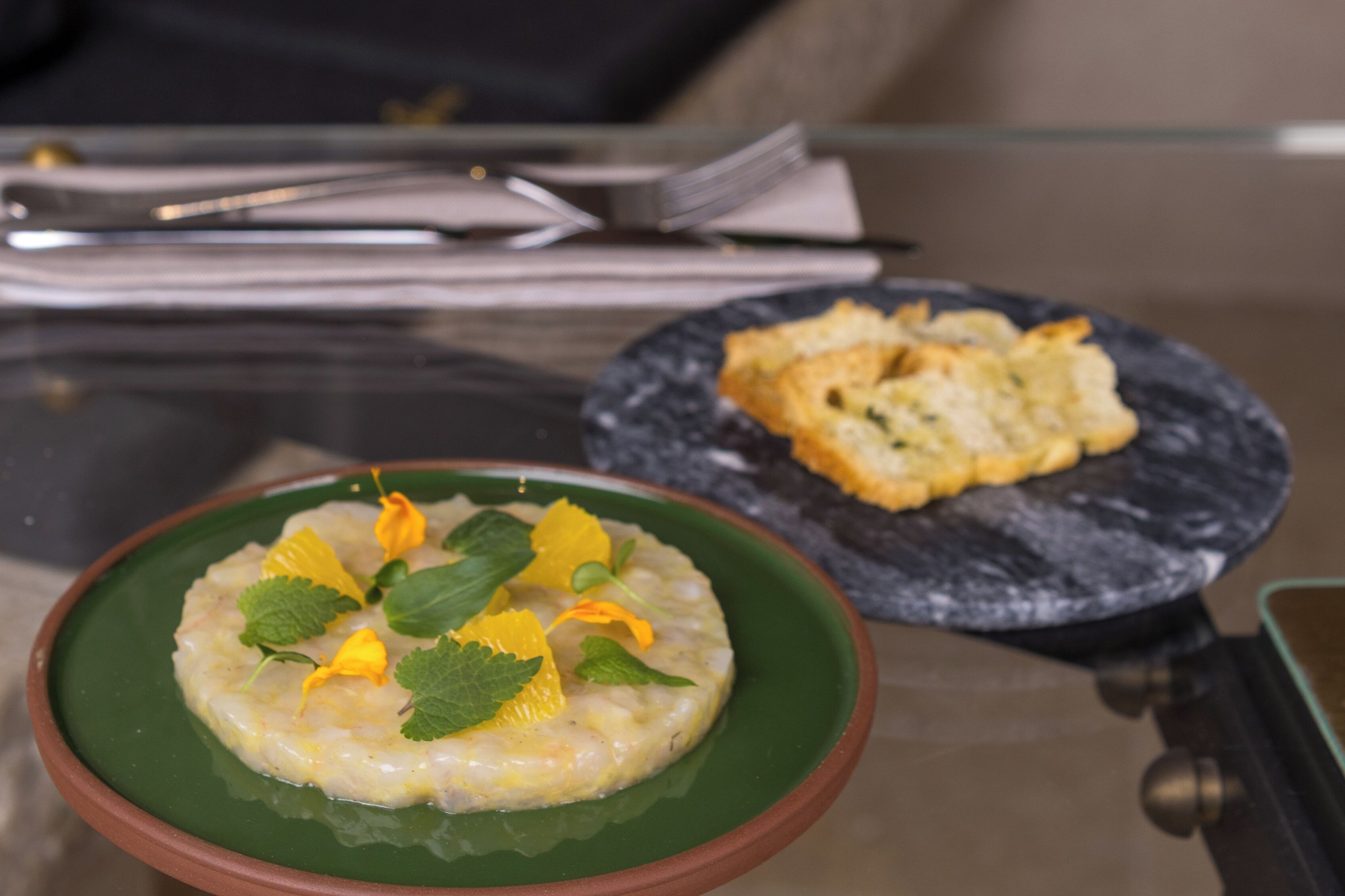 Una mesa con un bol verde de comida adornado con hierbas y un plato pequeño con un pastel.