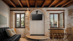 Un salon chaleureux avec un mur en pierre, un canapé noir et un téléviseur à écran plat fixé au mur.