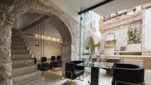 Un intérieur moderne avec un escalier menant à une salle à manger, des murs en pierre et une cloison en verre.