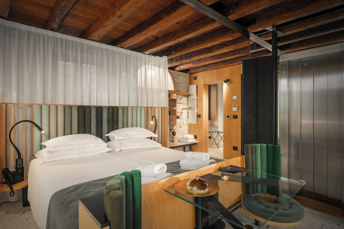 Habitación de hotel con cama, escritorio, silla, teléfono y ascensor.