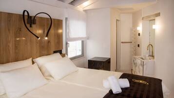 A hotel room with a wooden headboard, a large bed with white linens, a bedside table with a lamp, and a bathroom with a marble vanity and mirror.