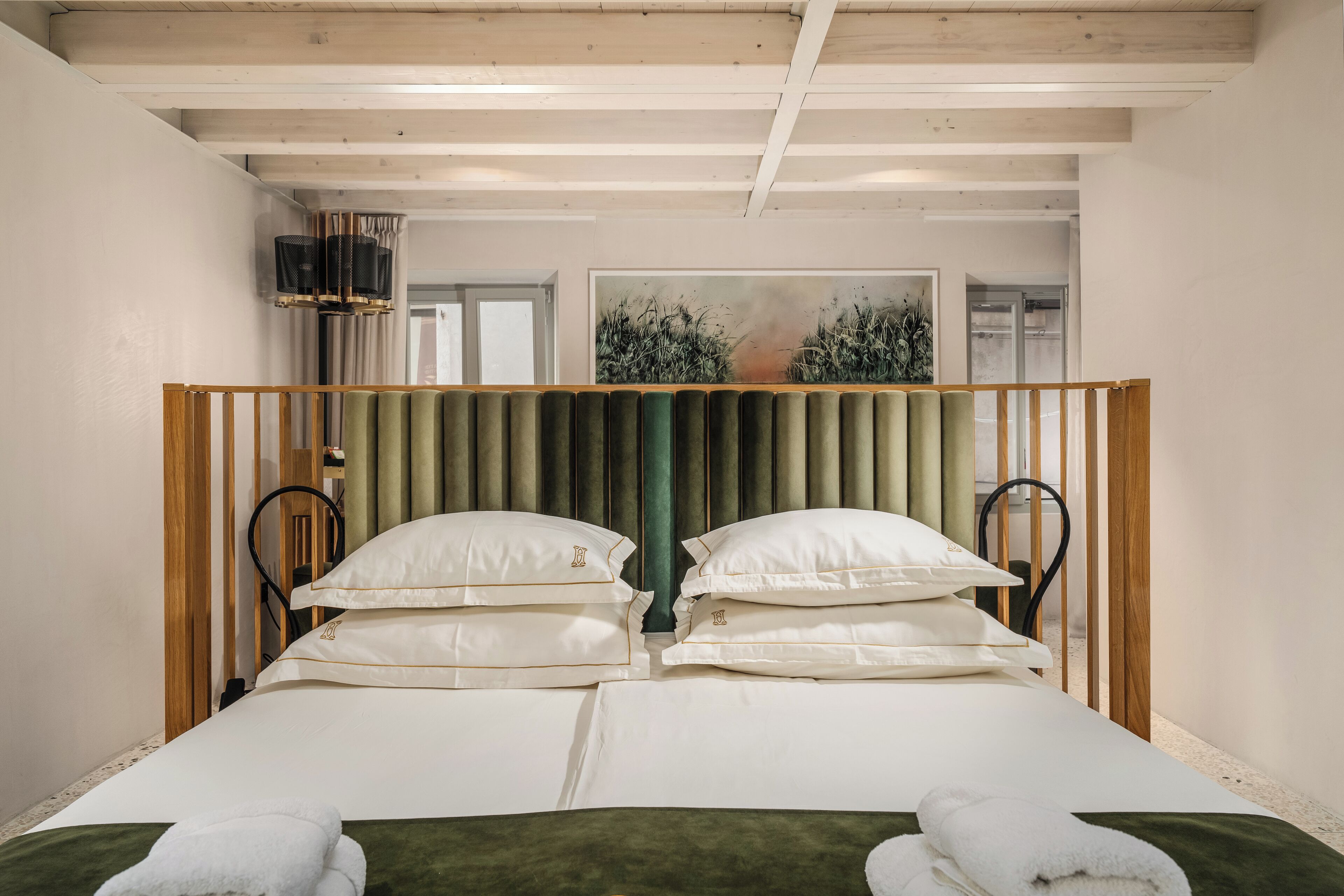 Una cama doble con cabecera verde, sábanas blancas y dos almohadas.