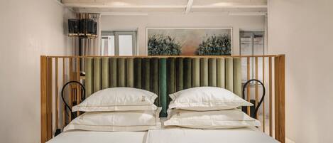 Una cama doble con cabecera verde, sábanas blancas y dos almohadas.