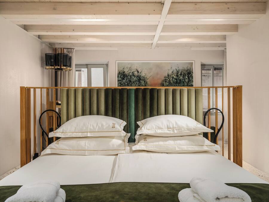 Una cama doble con cabecera verde, sábanas blancas y dos almohadas.