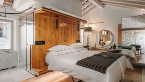 Une chambre moderne avec une tête de lit en bois, un grand lit recouvert de linge de maison blanc, une table de chevet avec une lampe et un grand miroir.