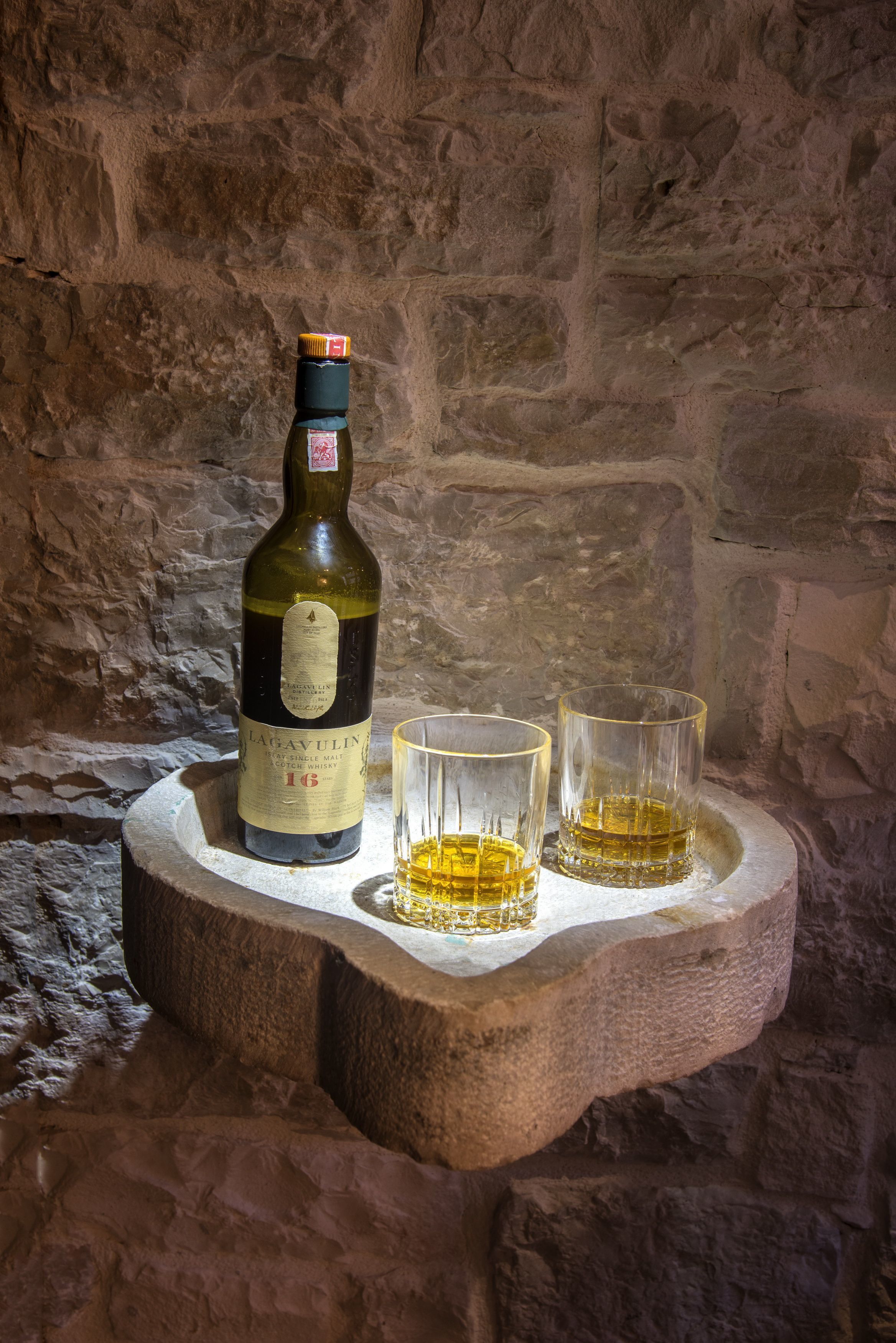 A bottle of Lagavulin 16 whisky on a stone tray with two glasses of whisky.