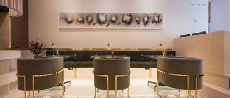 A modern reception area with a marble floor, a large abstract painting, and three dark grey stools with gold accents.