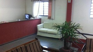 A reception area with a reception desk, a sofa, a striped chair, and a potted plant. - Hotel 50 (Extrema)