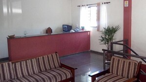 A reception area with a red counter, a computer, and two striped sofas. - Hotel 50 (Extrema)