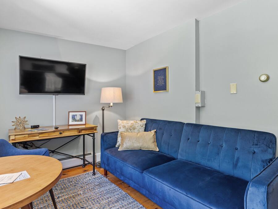 Uma sala de estar moderna com um sofá azul, uma escrivaninha de madeira, uma TV de tela plana e um abajur.