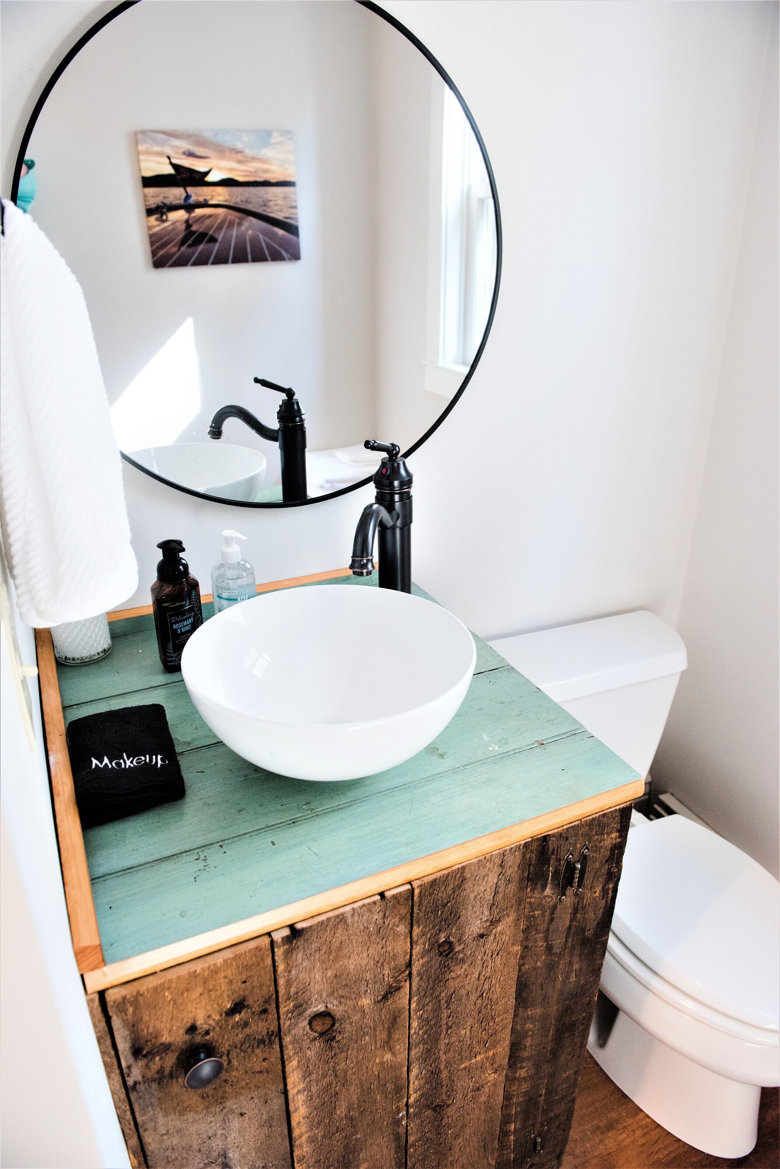 A bathroom with a white sink, black faucet, and a round mirror above it.