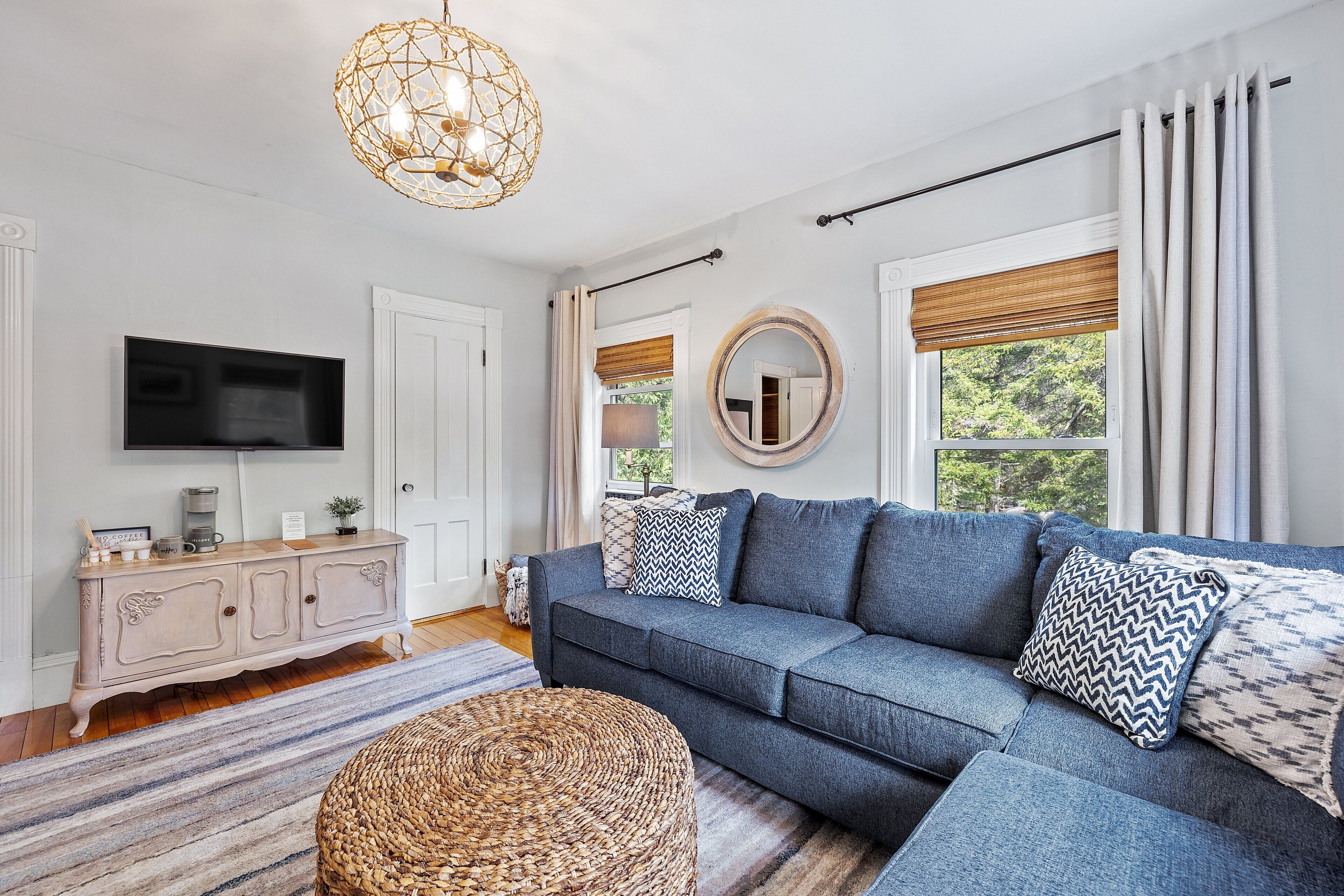 A living room with a sectional sofa, a television, a cabinet, and a large window with curtains.