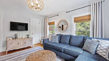 A living room with a sectional sofa, a television, a cabinet, and a large window with curtains.