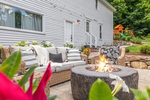 A patio with a stone fire pit, outdoor furniture, and a play structure in the background. - Inn On Golden Pond (Holderness)